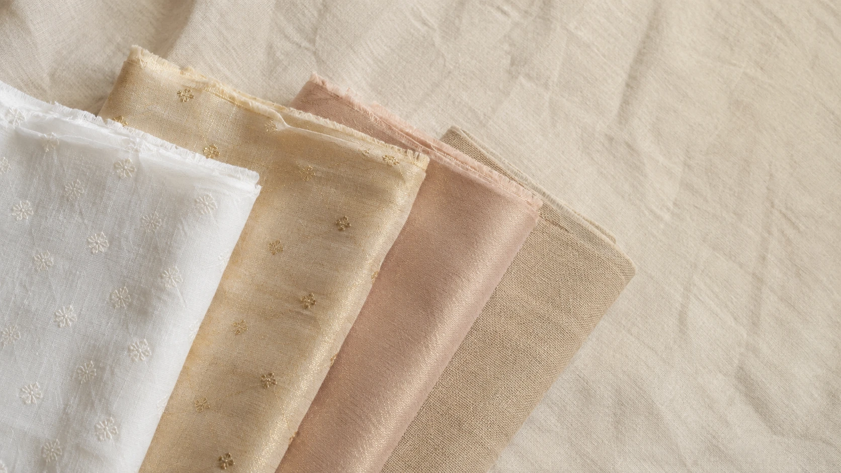 Folded cotton, chanderi, tissue and linen unstitched suit fabrics arranged on ivory linen